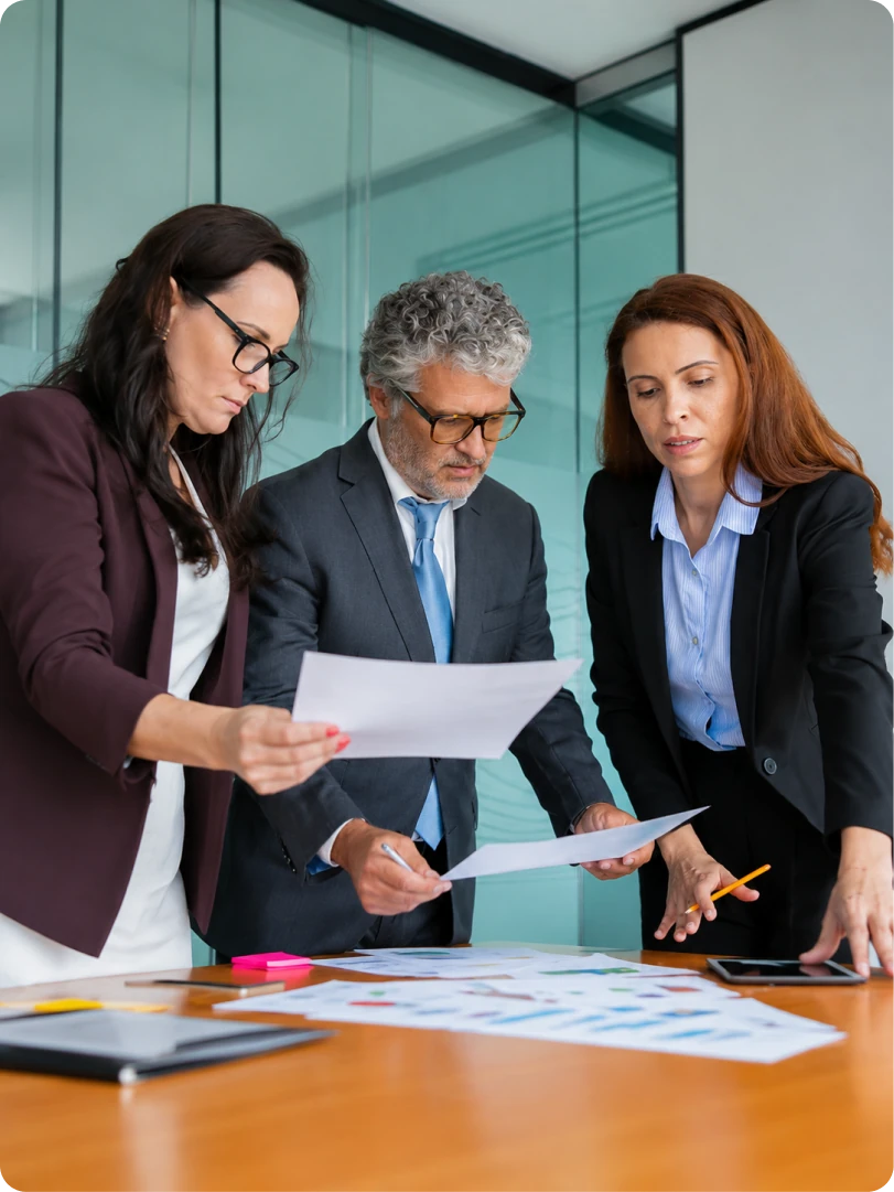 Three category managers comparing printed category reports across a meeting table